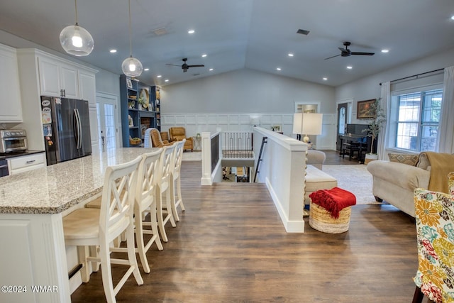 kitchen featuring dark stone counters, open floor plan, freestanding refrigerator, a kitchen bar, and pendant lighting