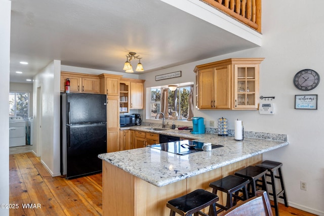 kitchen with a breakfast bar area, a peninsula, a sink, black appliances, and glass insert cabinets