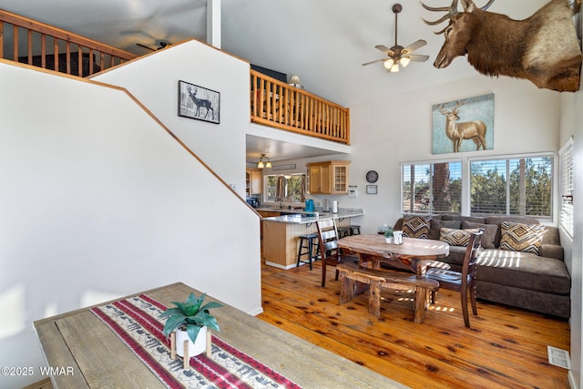 living room with a towering ceiling, light wood-type flooring, visible vents, and a ceiling fan