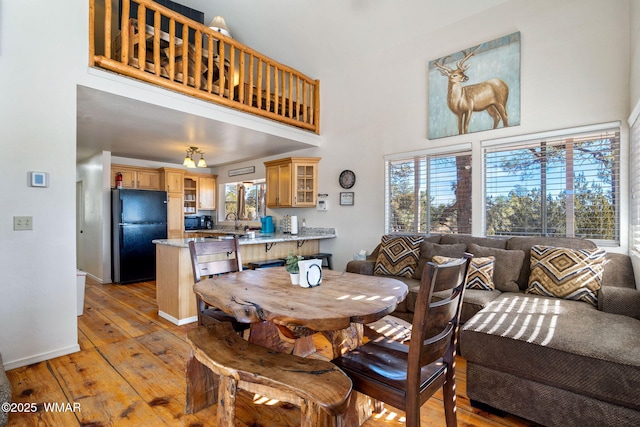 dining space with a towering ceiling, light wood-style floors, and baseboards