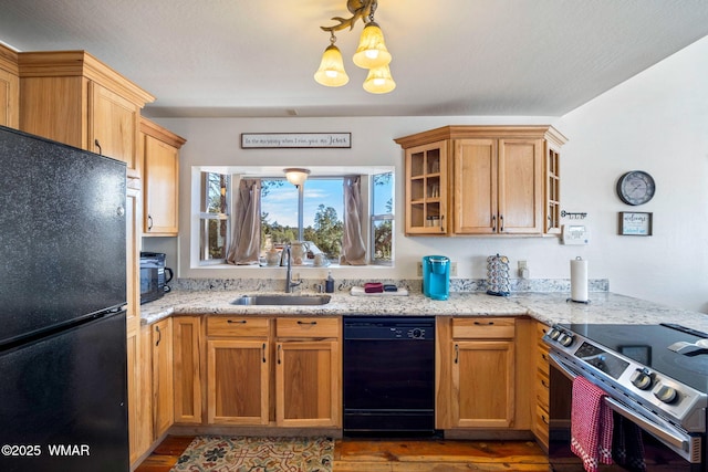 kitchen featuring light stone counters, wood finished floors, a sink, black appliances, and glass insert cabinets