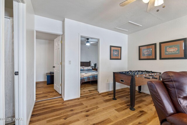 recreation room with a ceiling fan, attic access, baseboards, and wood finished floors