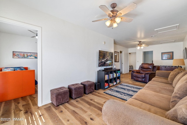 living room with visible vents, a ceiling fan, light wood-style flooring, and attic access