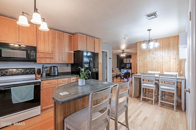 kitchen featuring black appliances, dark countertops, a chandelier, light wood finished floors, and wood walls