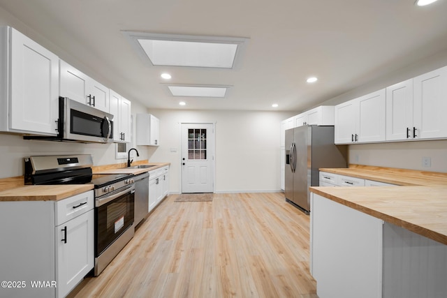 1259 S Penrod Dr, Pinetop, AZ 85935 - kitchen featuring butcher block countertops, appliances with stainless steel finishes, light wood-type flooring, a skylight, and white cabinetry