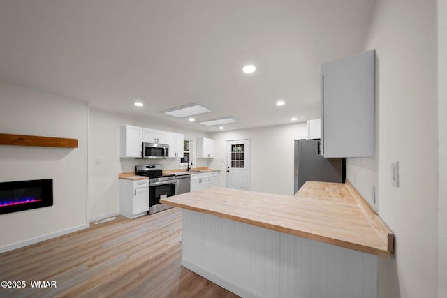 1259 S Penrod Dr, Pinetop, AZ 85935 - kitchen with appliances with stainless steel finishes, a peninsula, light wood-style floors, white cabinets, and a glass covered fireplace