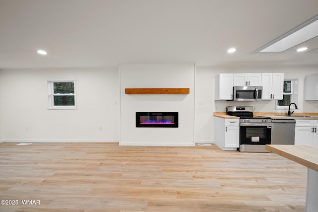 1259 S Penrod Dr, Pinetop, AZ 85935 - kitchen featuring appliances with stainless steel finishes, white cabinetry, light wood-style flooring, recessed lighting, and a glass covered fireplace