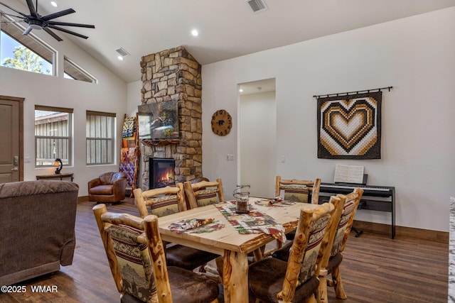 dining area featuring ceiling fan, wood finished floors, vaulted ceiling, and a stone fireplace