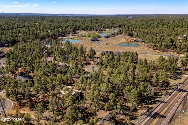 aerial view of property and surrounding area featuring a heavily wooded area and a nearby body of water