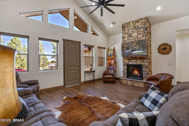 living room featuring a ceiling fan, wood finished floors, healthy amount of natural light, a stone fireplace, and high vaulted ceiling