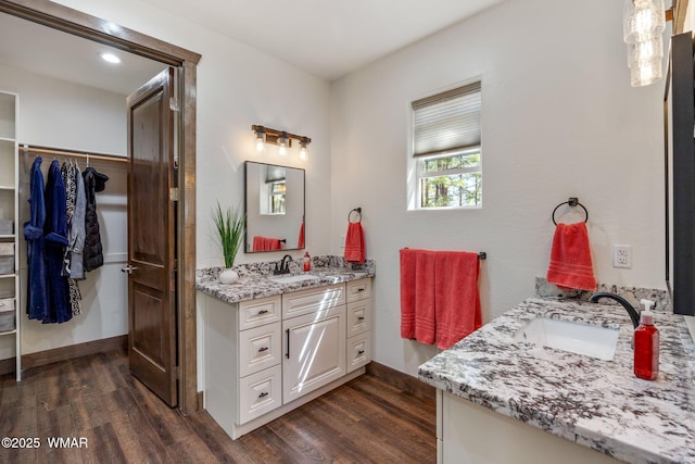bathroom with wood finished floors, two vanities, a walk in closet, and baseboards