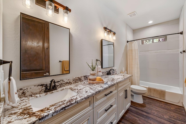 bathroom featuring toilet, wood finished floors, double vanity, and shower / tub combo