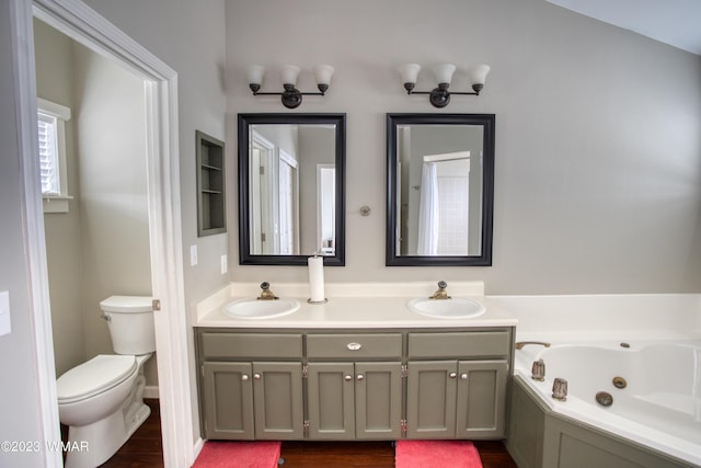 full bathroom with double vanity, a tub with jets, toilet, and a sink