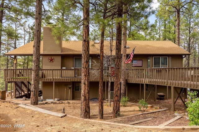 view of front facade with a shingled roof, a wooden deck, and stairway