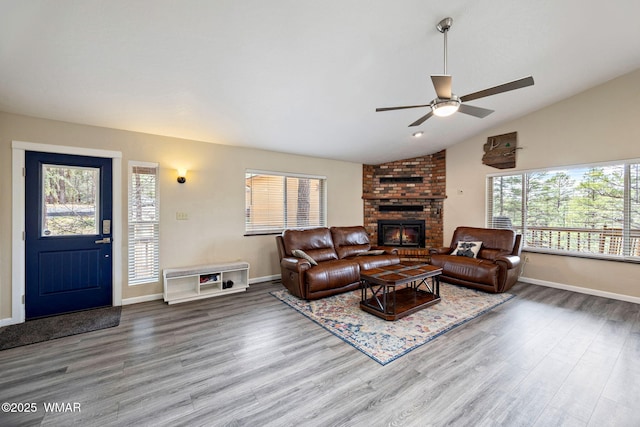 living area with ceiling fan, a fireplace, vaulted ceiling, wood finished floors, and baseboards