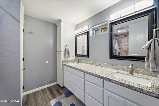 bathroom featuring wood finished floors, double vanity, a textured ceiling, and baseboards