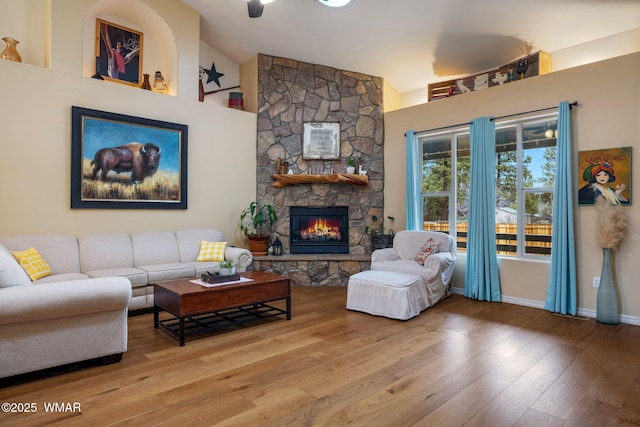 living room with a stone fireplace, high vaulted ceiling, baseboards, and hardwood / wood-style flooring