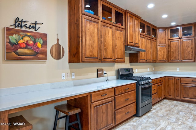 kitchen featuring under cabinet range hood, brown cabinets, glass insert cabinets, and stainless steel range with gas cooktop