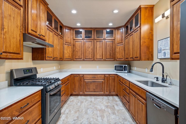 kitchen featuring under cabinet range hood, appliances with stainless steel finishes, brown cabinetry, and a sink