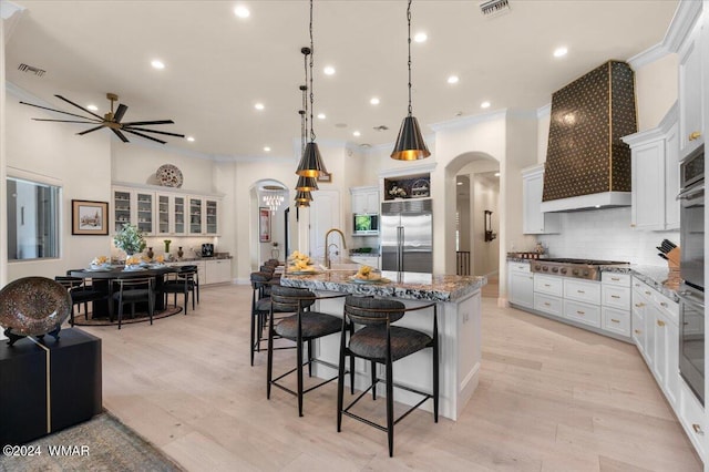 kitchen with arched walkways, stainless steel appliances, white cabinets, light stone countertops, and a large island with sink