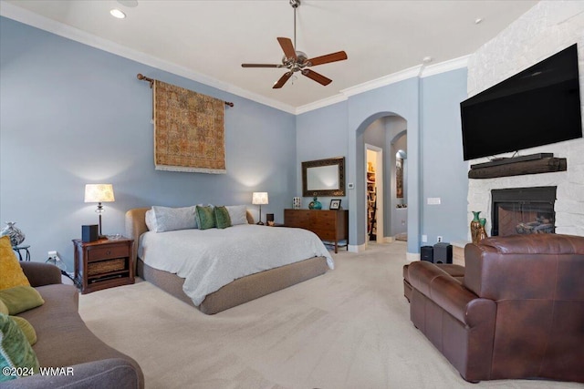 bedroom featuring arched walkways, crown molding, light colored carpet, ceiling fan, and a stone fireplace