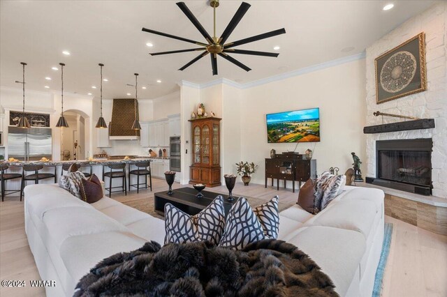 living room with arched walkways, ornamental molding, light wood-style floors, a fireplace, and recessed lighting