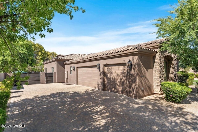 mediterranean / spanish home with a garage, decorative driveway, a tile roof, and stucco siding