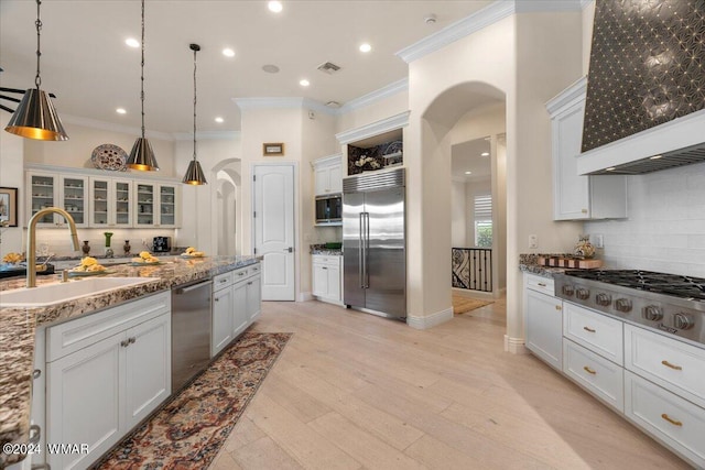 kitchen with built in appliances, arched walkways, a sink, white cabinetry, and hanging light fixtures