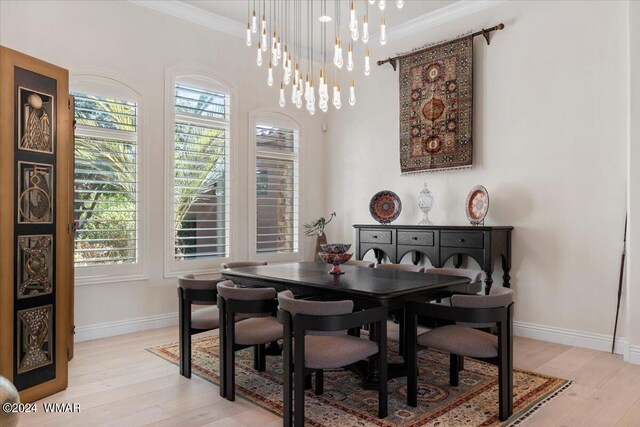 dining space with light wood-type flooring, baseboards, ornamental molding, and a notable chandelier