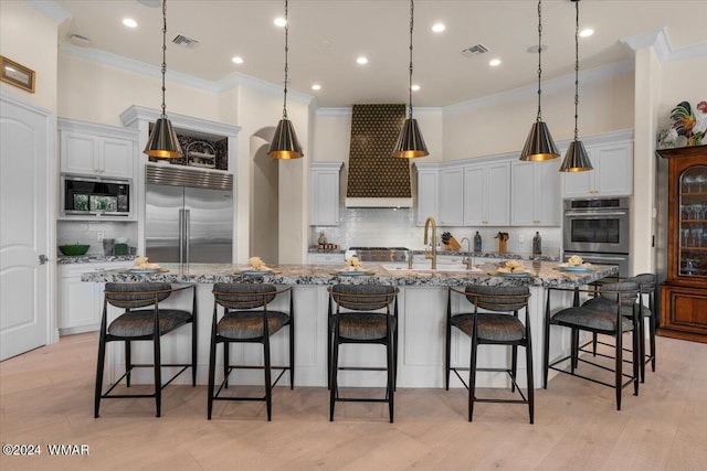 kitchen featuring built in appliances, a large island, a breakfast bar area, and light stone countertops