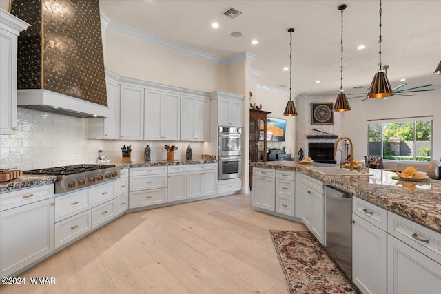 kitchen with stainless steel appliances, premium range hood, a sink, white cabinetry, and pendant lighting