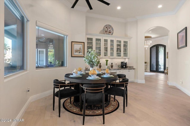 dining area featuring arched walkways, french doors, crown molding, and light wood finished floors