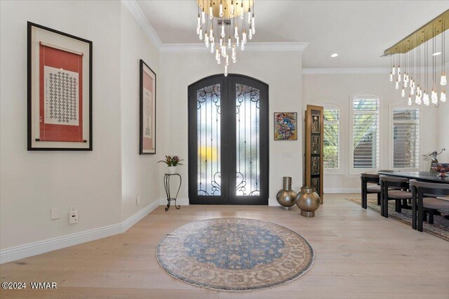 foyer entrance featuring light wood-style floors, french doors, a notable chandelier, and ornamental molding