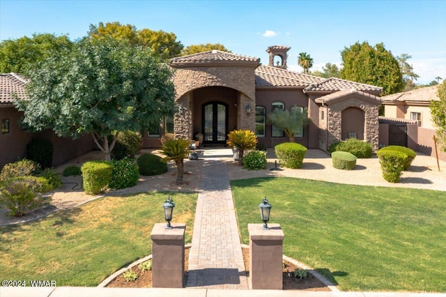 mediterranean / spanish-style home with french doors, stucco siding, stone siding, a tiled roof, and a front lawn