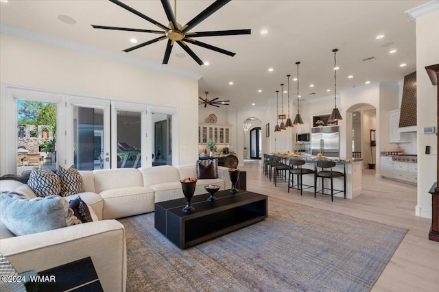 living area with arched walkways, ornamental molding, light wood-style flooring, and a ceiling fan