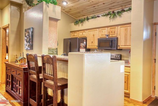 kitchen with freestanding refrigerator, light brown cabinetry, light wood-style floors, a kitchen bar, and wooden ceiling