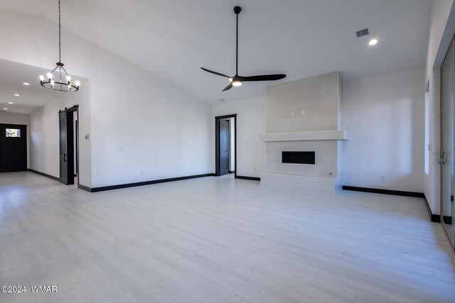 unfurnished living room with light wood-style flooring, a tiled fireplace, a barn door, ceiling fan, and baseboards