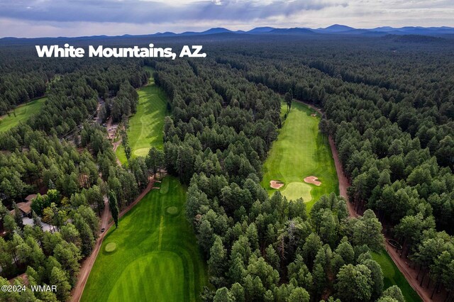 aerial view with view of golf course, a mountain view, and a view of trees