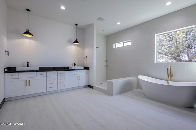 bathroom featuring double vanity, a soaking tub, wood finished floors, a sink, and a walk in shower