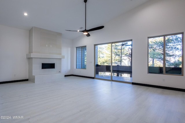 unfurnished living room with light wood-style flooring, a fireplace, high vaulted ceiling, and baseboards