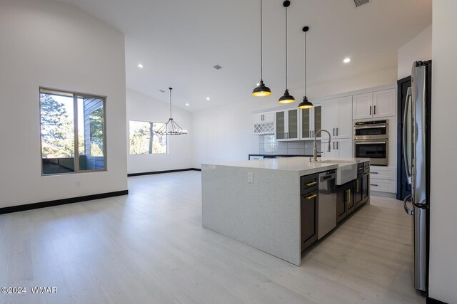 kitchen featuring stainless steel appliances, a sink, white cabinets, an island with sink, and glass insert cabinets