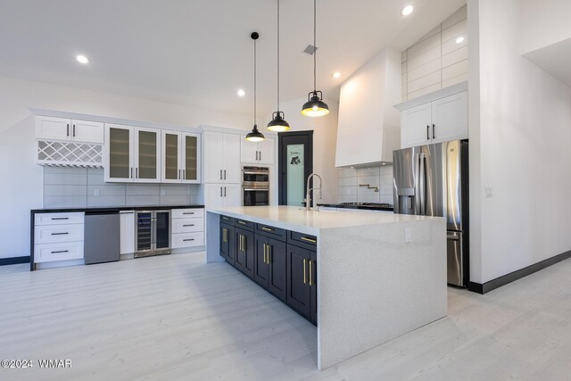 kitchen featuring beverage cooler, glass insert cabinets, stainless steel appliances, white cabinetry, and pendant lighting