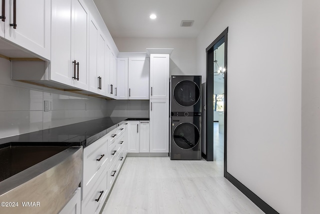 kitchen with stacked washer and clothes dryer, light wood finished floors, dark countertops, decorative backsplash, and white cabinets