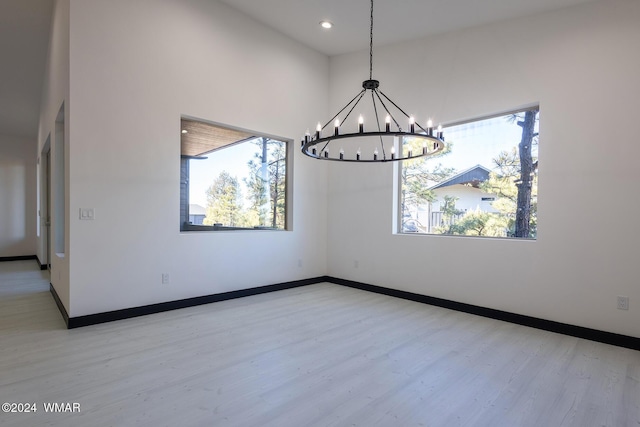 empty room featuring recessed lighting, a notable chandelier, light wood-style flooring, and baseboards