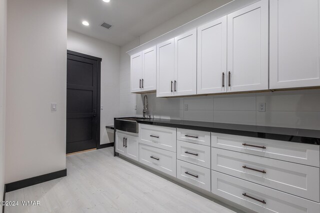 kitchen featuring visible vents, dark countertops, light wood-style floors, white cabinetry, and a sink