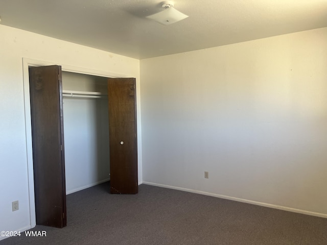 unfurnished bedroom with baseboards, dark carpet, and a closet