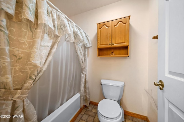 full bath with shower / bath combo with shower curtain, toilet, baseboards, and stone finish floor