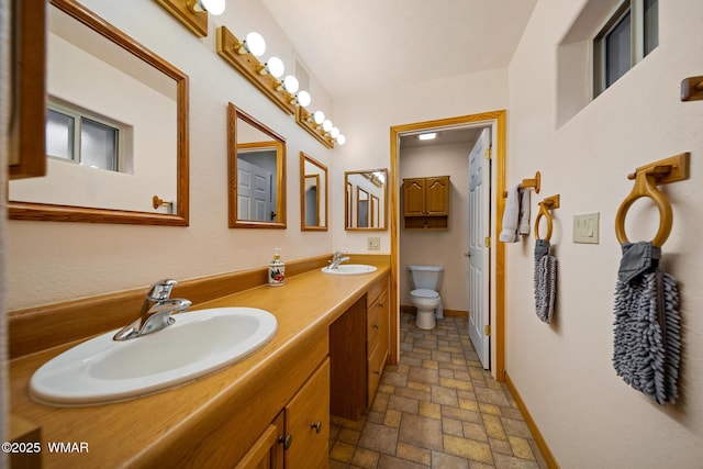full bath featuring a sink, double vanity, toilet, and stone tile flooring