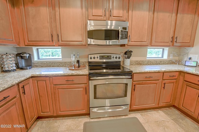 kitchen with appliances with stainless steel finishes, brown cabinetry, and light stone countertops