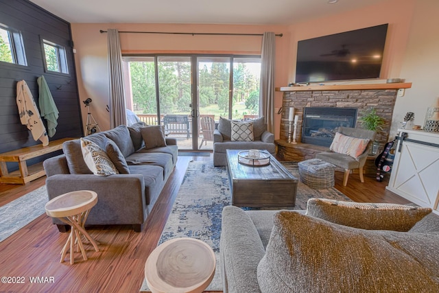 living area featuring wood walls, wood finished floors, and a stone fireplace